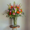 Tall arrangement of pink roses, orange gerbera daisies, lilies and snapdragons in a clear glass vase