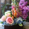 Mixed bouquet of pink roses, orange tulips, and purple blooms in a dark container