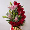 Red roses and pink lilies in a pink vase with gold-wrapped chocolates