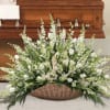 White floral spray in a wicker basket in front of a wooden casket