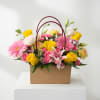 Mixed pink and yellow flowers arranged in a brown handled box