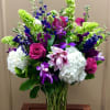 Tall mixed bouquet with pink roses, white hydrangeas, and purple orchids in a glass vase