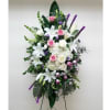 Tall standing spray of white lilies, hydrangeas, and pink roses with purple accents on an easel