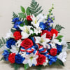 Patriotic arrangement of white lilies, red roses, and blue flowers with a red, white, and blue ribbon