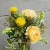 Yellow roses and spiky yellow blooms with green pods in a clear glass vase