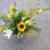 Loose mixed bouquet with sunflowers, white lilies and yellow daisies in a clear glass vase