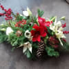 Low winter centerpiece with red amaryllis, white poinsettias, berries, and pinecones in dense evergreen foliage