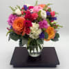 Bright mixed bouquet of roses, carnations, and hydrangeas in a round clear glass vase