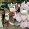 Three plush unicorn toys sit beside potted plants.