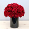 Compact arrangement of red roses in a glossy black cylinder vase