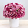 Dome-shaped arrangement of pink and magenta roses in a white cylinder vase