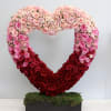 Large open heart of pink and red roses on a moss-covered base in a rectangular black container