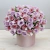 Round arrangement of pale lavender roses and pink orchids in a light pink hat box container.