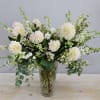 Tall arrangement of cream dahlias and white flowers in a clear textured glass vase