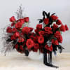 Asymmetrical arrangement of red roses with red carnations and black foliage in a white bowl vase