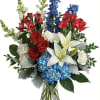 Mixed bouquet of red roses, white lilies, blue hydrangeas, and red blooms in a glass vase
