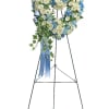Heart-shaped floral wreath on a stand with blue and white flowers and a ribbon