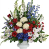 Mixed red, white, and blue floral arrangement in a white pedestal vase