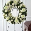 White floral funeral wreath on a black stand beside a casket