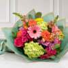Mixed bouquet of pink, orange, yellow, and green flowers wrapped in teal paper