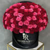 Large round arrangement of pink and red roses in a black hat box