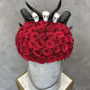 Red roses arranged in a gray hat box with black horn decorations and skull toppers