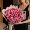 Woman holding a large bouquet of pink roses wrapped in pale paper