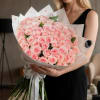 Woman holding a large bouquet of pale pink roses wrapped in white paper