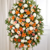 Tall standing spray with orange lilies, white mums, peach roses, and carnations on a leafy easel.