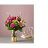 Mixed pink lilies, roses, carnations, and green hydrangea in a clear vase with gold base on a tabletop
