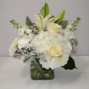 Compact white and ivory bouquet of roses, lilies, and hydrangeas in a clear glass cube vase
