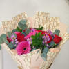 Hand-tied bouquet of red roses and pink gerbera daisies wrapped in branded cream paper