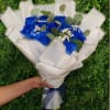 Handheld bouquet of vivid blue roses and white filler flowers wrapped in white paper