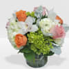 Round arrangement of orange and pink roses, white orchids and hydrangeas in a clear glass vase