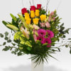 Tall mixed bouquet of red and yellow roses, pink lilies and gerberas in a white vase