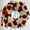 Standing wreath of red roses, white daisies, and green-tinted mums on a black easel with red ribbon bow