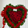Heart-shaped standing wreath of red roses and carnations with greenery and a red ribbon