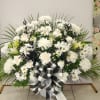 Large white floral spray with daisies, roses, and a black-and-white ribbon bow