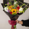 Mixed bouquet with a sunflower, roses, and white blooms wrapped in black paper