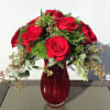 Red roses arranged in a red glass vase with greenery