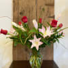 Tall arrangement of red roses and light pink lilies in a clear glass vase