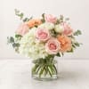 Pink roses, white hydrangea, and peach carnations in a clear glass vase