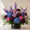 Mixed bouquet of roses, hydrangeas, and purple blooms in a black vase