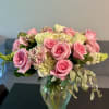 Pink roses and pale flowers arranged in a glass vase