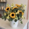 Sunflowers and pale yellow flowers arranged in a white vase