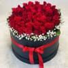 Red roses arranged in a round black box with a red ribbon.