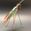 Metal wire grasshopper sculpture with a green body on a dark background