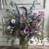 Mixed bouquet of blue, pink, and white flowers in a clear glass vase