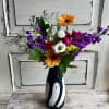 Mixed bouquet with orange gerberas, purple flowers, and roses in a black vase