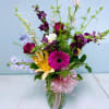 Mixed bouquet in a glass vase with pink ribbon and bright gerbera, lilies, and snapdragons